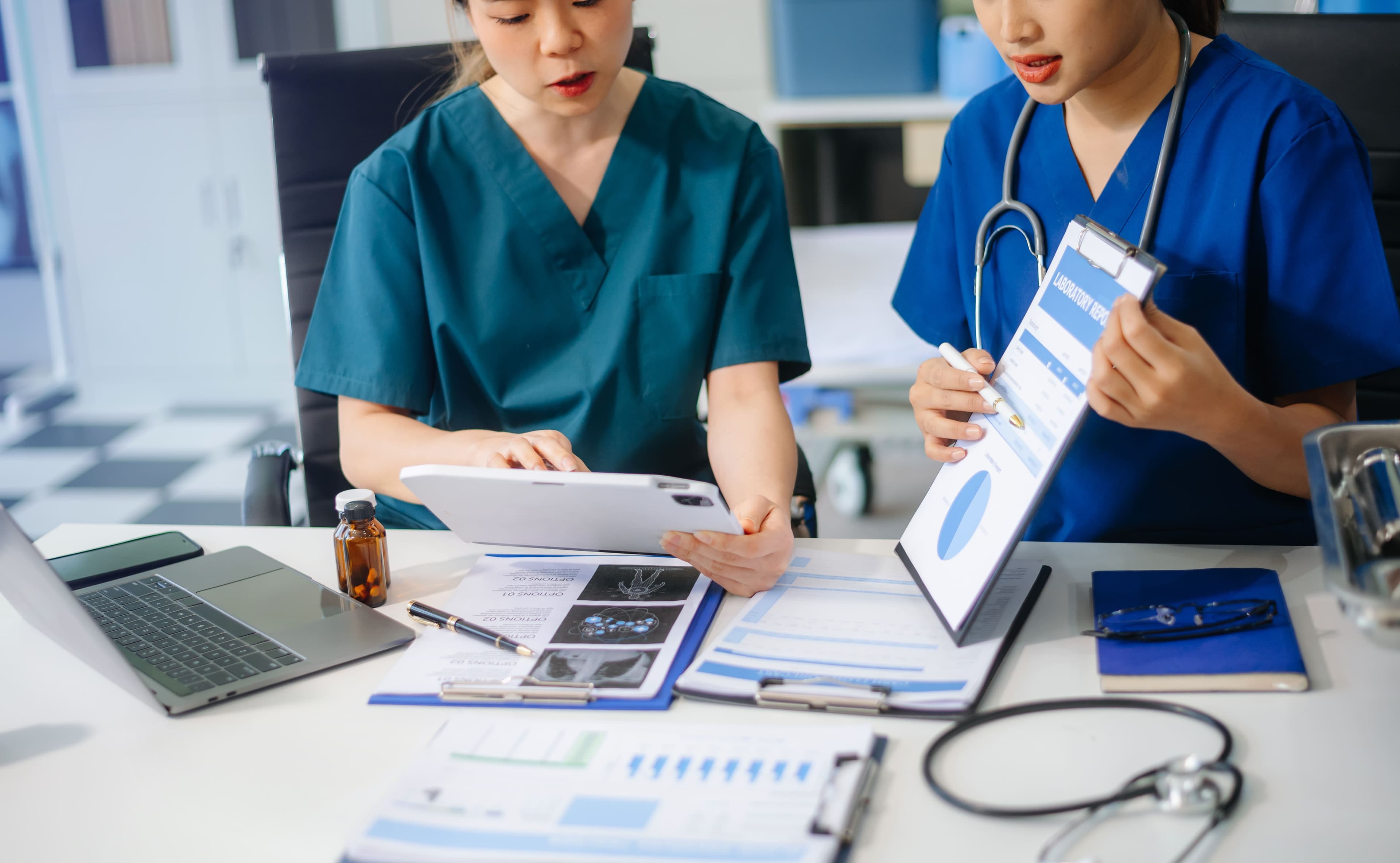 Two clinicians in scrubs reviewing lab reports and charts together at a desk